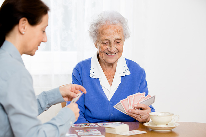 Ältere Dame beim Kartenspielen mit Pflegerin